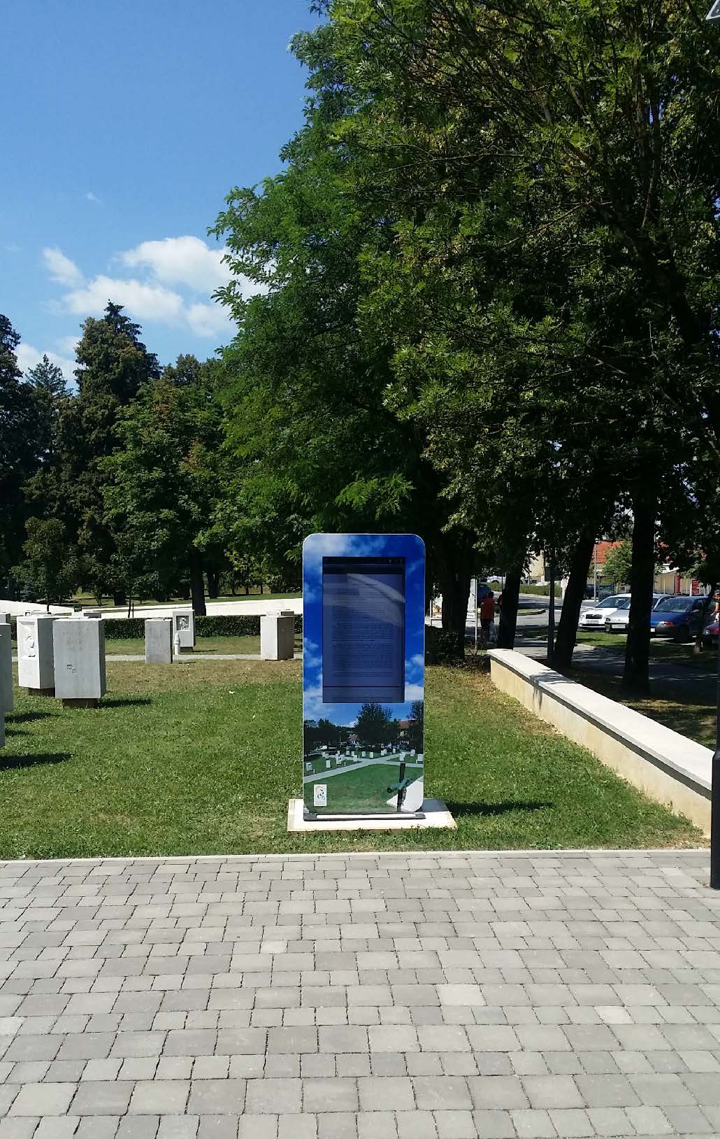 Digital display (info kiosk totem) in a park with trees and a clear sky